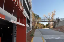 Thumbnail for Parking garage entrance with clearance height sign next to a road leading to a pedestrian bridge over the street.