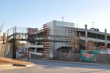 Thumbnail for Modern multi-level parking garage with decorative panels and pedestrian bridge over street at sunset.