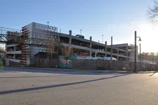 Thumbnail for Multi-level parking garage with string lights and wooden fence under a clear blue sky during daytime.
