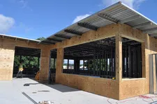 Thumbnail for Construction site showing wood and metal framework of a building under clear blue sky with a worker in safety vest.