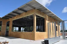 Thumbnail for Construction site with wooden framing and metal beams under a clear blue sky, showing early building stages.