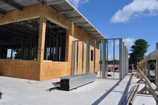 Thumbnail for Construction site showing wooden framing and metal studs being installed under a clear blue sky.