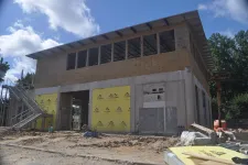 Thumbnail for Two-story concrete and wood building under construction with metal roof and surrounding construction materials.