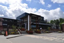 Thumbnail for Modern commercial building with outdoor seating, coffee shop, and clear skies with scattered clouds.