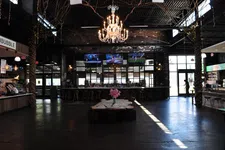 Thumbnail for Spacious modern bar with wooden accents, chandelier, multiple TVs, and pink flower centerpiece on large wooden table.