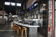 Thumbnail for Modern bar interior with wooden stools, concrete countertop, brick walls, and industrial pendant lighting.