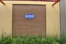 Thumbnail for Ross store sign mounted on wooden panel wall with surrounding beige walls and greenery below the sign