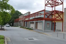 Thumbnail for Exterior view of a Joann fabric and craft store with red metal awnings and a tree-lined parking area.