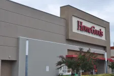 Thumbnail for Exterior view of HomeGoods store with large red sign and landscaping including flowering trees.