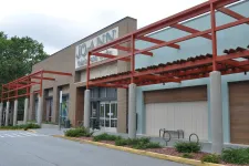 Thumbnail for Exterior of a Joann Fabrics and Crafts store with red metal framework and glass windows on a cloudy day
