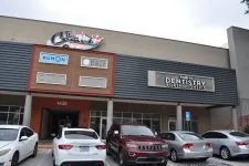Thumbnail for Exterior of a commercial building with signs for Kumon, Elite Golf, dentistry, and parked cars outside