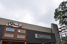 Thumbnail for Commercial building facade featuring signs for Kumon, Elite Fit Golf, dentistry, and other businesses under a cloudy sky.