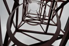 Thumbnail for View looking up through circular metal rings of a tall industrial tower against a cloudy sky