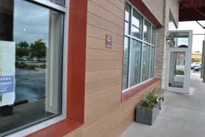 Thumbnail for Modern restaurant exterior with large windows, tan wood paneling, potted plants, and sidewalk seating area.