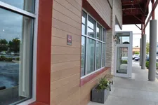 Thumbnail for Modern building exterior with large windows, planter box, and an entry door under a covered walkway.