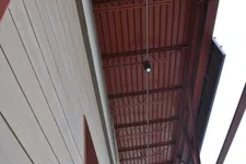 Thumbnail for View looking up at a modern building's red metal ceiling and adjacent light-colored wood panel wall with a ceiling light fixture.