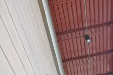 Thumbnail for Wood paneled wall beside a red industrial ceiling with exposed beams and a hanging spotlight.