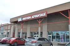 Thumbnail for Exterior view of Uniform Advantage store with cars parked in front under overcast sky.