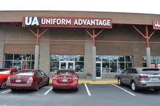 Thumbnail for Storefront of Uniform Advantage with red and gray vehicles parked in front under clear sky.