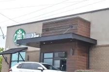 Thumbnail for Starbucks coffee shop exterior with drive-thru lane and a white SUV parked nearby during daytime.