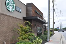 Thumbnail for Starbucks coffee shop exterior with drive-thru sign and landscaped greenery by busy street corner.