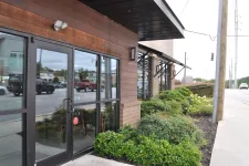 Thumbnail for Commercial building entrance with glass doors and landscaped greenery along the sidewalk on a busy street.