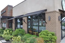 Thumbnail for Starbucks coffee shop exterior with large windows, black awnings, brick and wood facade, and green landscaping.