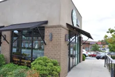 Thumbnail for Exterior view of a Starbucks coffee shop with brick walls, large windows, and outdoor greenery near a parking lot.