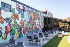 Thumbnail for Outdoor patio with modern tables and chairs next to a colorful butterfly mural on a brick wall under clear sky