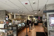 Thumbnail for Interior of a cafe with pastry displays, customers in line, menu boards, and warm tile flooring under ceiling lights