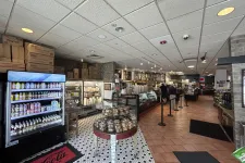 Thumbnail for Interior of a bakery cafe with display cases, beverage fridge, baked goods table, and customers ordering at counter.