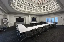Thumbnail for Modern conference room with U-shaped white tables, rolling chairs, and a decorative domed ceiling with lights.