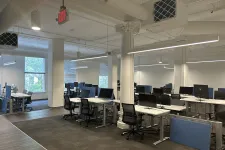 Thumbnail for Modern office space with multiple desks, black chairs, and computer monitors under bright lighting and large windows.