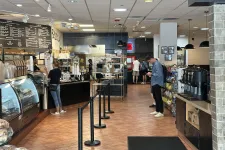 Thumbnail for Spacious cafe interior with customers ordering, menu boards, snack shelves, and coffee station with tiled floor.