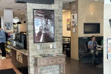 Thumbnail for Interior of a cafe with brick walls, framed Brooklyn poster, coffee station, and a man dining at a booth.