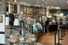 Thumbnail for Cozy bakery interior with bread display, glass cases, menu boards, and customer ordering at counter.