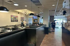 Thumbnail for Interior of a casual restaurant with black booth seating, hanging lamps, colorful wall art, and tile floors.