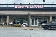 Thumbnail for Brooklyn Bagel & Deli storefront with outdoor seating and customers, black truck parked nearby.