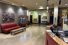 Thumbnail for Modern reception area with red couch, wooden bench, fish tank, and curved wood desk with computers.