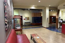 Thumbnail for Bright lobby area with a red leather couch, rustic wooden table, aquarium, and modern lighting fixtures.