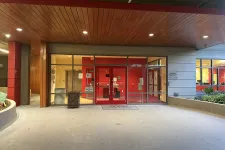 Thumbnail for Entrance to a modern building with red doors, glass panels, wooden ceiling, and concrete floor at dusk