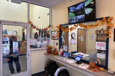Thumbnail for School office entrance decorated with autumn leaves, pumpkins, security monitors, and visitor check-in tablets.