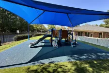Thumbnail for Outdoor playground with slides and climbing structures shaded by large blue canopy on sunny day.