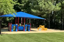 Thumbnail for Children's playground with blue and red play structure under large blue canopy and yellow slide on green turf.