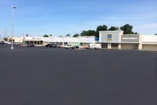Thumbnail for Wide empty parking lot in front of a strip mall featuring Aldi Food Market and other stores under clear blue sky