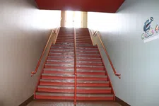 Thumbnail for Red metal staircase with handrails on both sides leading up to a bright doorway with a colorful wall sticker.