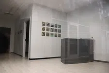Thumbnail for Minimalist office with light wood flooring, white walls, small wall art, and a dark wooden desk or cabinet.