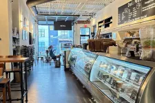 Thumbnail for Bright modern deli interior with glass display cases, seating area, and a person sitting near the entrance.