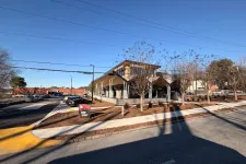 Thumbnail for Modern restaurant building with large windows under clear blue sky and parking lot on a sunny day.