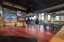 Thumbnail for Modern sports bar with large screens showing games, industrial ceiling, wooden benches, and people near the bar counter.